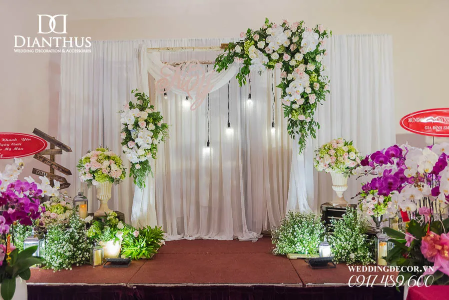 Không gian tiệc cưới ngoài trời với backdrop hoa tươi và ánh sáng vàng ấm