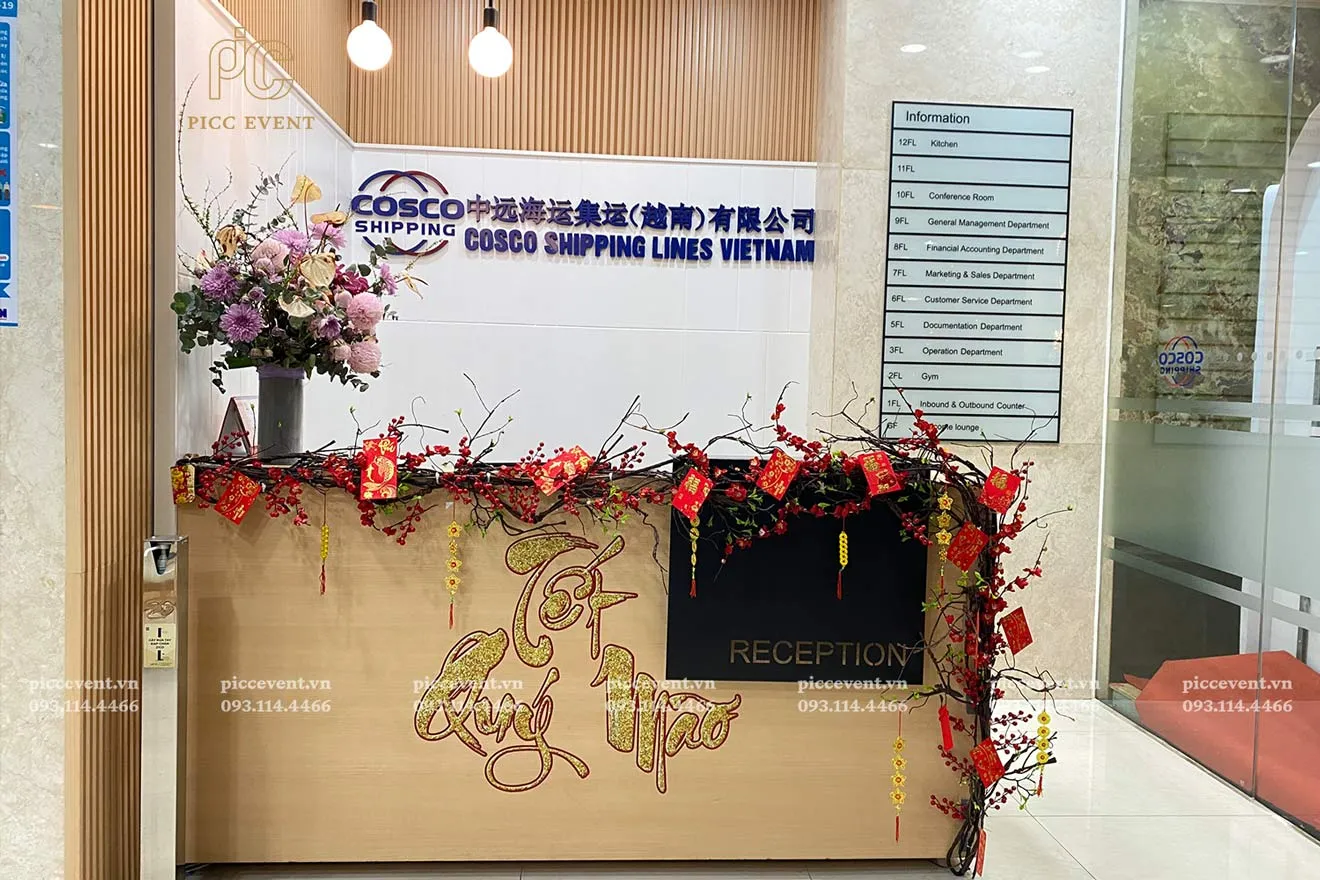 Quầy lễ tân được trang trí với hoa tươi, lồng đèn và backdrop đỏ vàng
